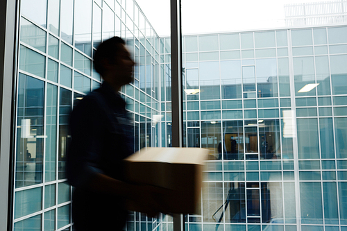 Defocused courier with package walking along modern office building window inside