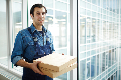 Staff of pizza delivery service with two food packs standing by window inside contemporary office center