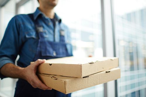 Two boxes with fast food being carried by delivery man in uniform for one of clients