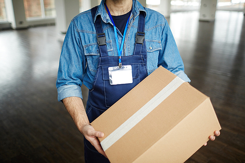 Midsection of delivery service worker in uniform carrying unpacked box to client