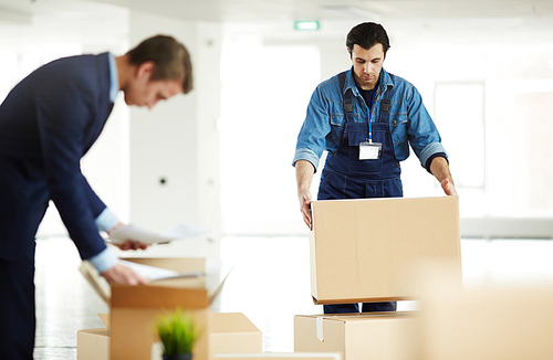 Relocation service worker putting packed box on top of another one while helping to carry packages