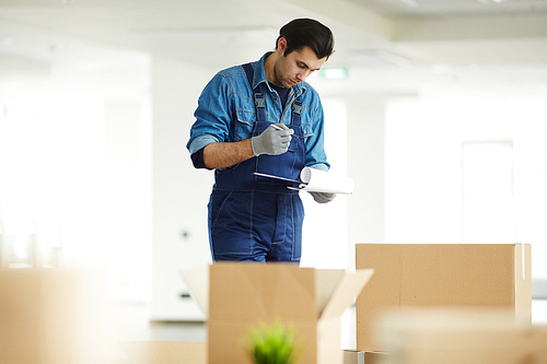 Young courier in uniform checking signature of client in receiving document over open box