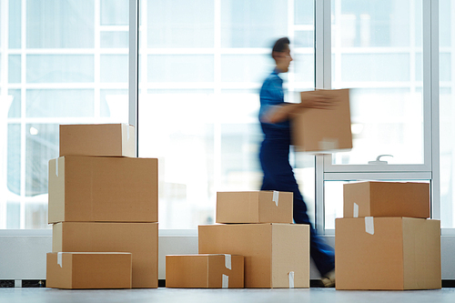 Blurred motion of contemporary worker with packed box walking to new office while delivering it to client