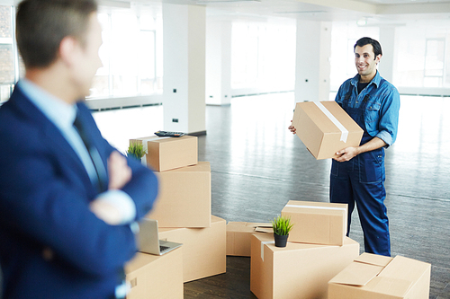 Young worker of distribution center helping director of business organization load packed boxes during relocation to new office