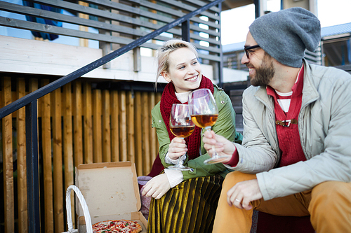 Young beautiful Caucasian couple clinking wine glasses and smiling happily while spending autumn day with food and drinks outdoors