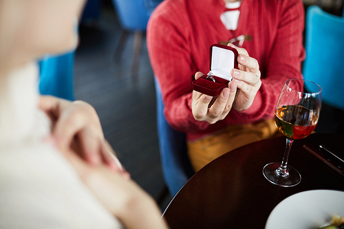 Close-up view of unrecognizable man proposing to his girlfriend with beautiful ring while having romantic date in restaurant