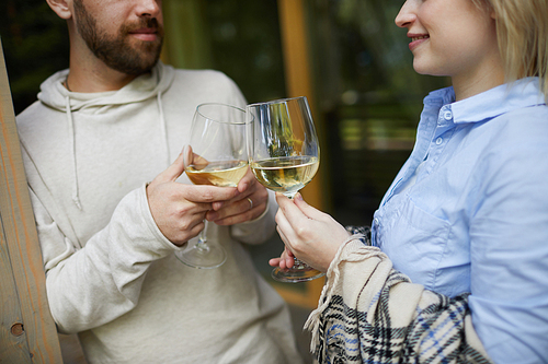 Crop shot of amorous Caucasian couple clinking glasses of white wine and looking at each other tenderly while celebrating anniversary