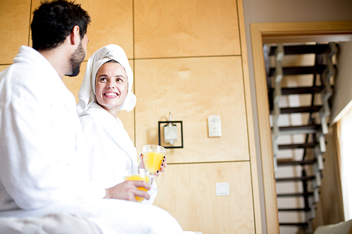 Smiling young woman with glass of drink looking at her husband during talk after bath