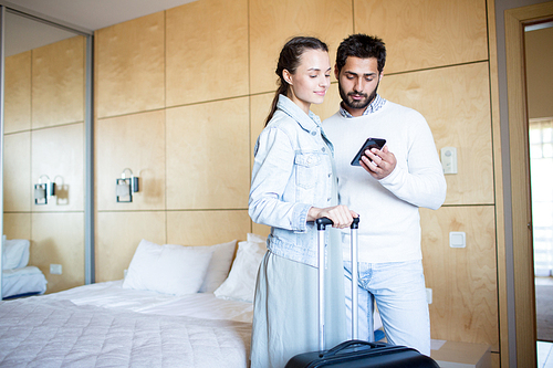 Young couple with suitcase searching for nearest flights in the net while leaving hotel room