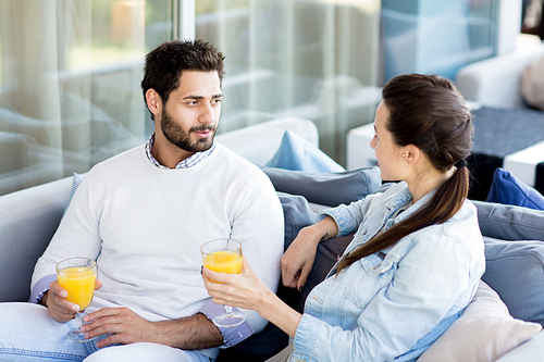 Young amorous man and woman with glasses of juice having rest in cafe and talking