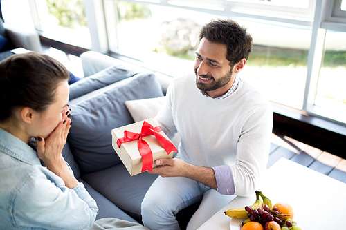 Young man giving box with present to his wife while celebrating anniversary in hotel cafe