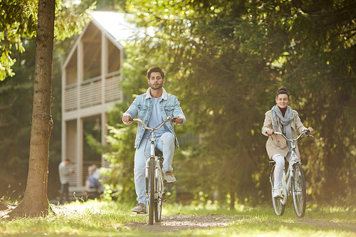 Leisure in country: positive young couple of cyclists having fun on warm autumn day and riding bikes in forest