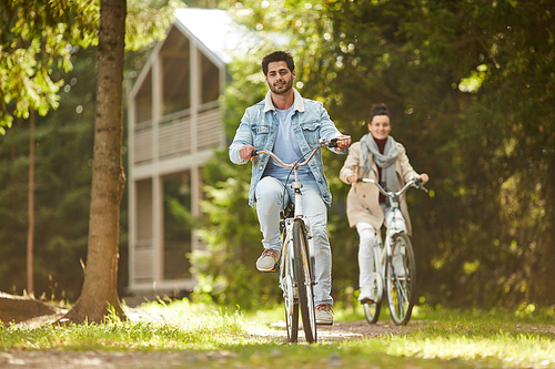 Cheerful carefree adult couple riding bike in country and enjoying warm autumn day together, they racing each other