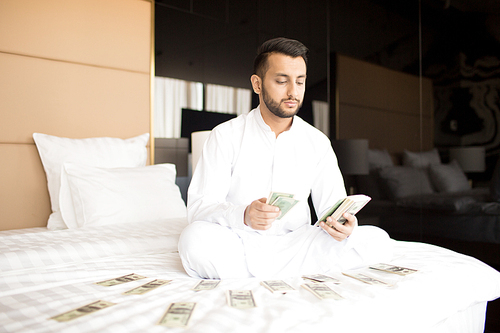 Cross-legged businessman in white clothes counting his money or salary while sitting on bed