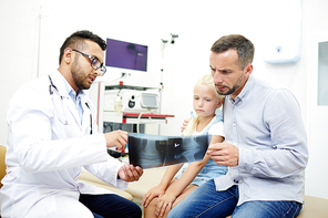 Doctor showing x-ray images of little girl to her father in hospital office