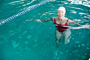 Mature woman in swimwear swimming in pool of contemporary leisure center