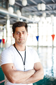 Young swimming instructor with crossed arms  with pool on background