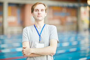 Young serious trainer with his arms crossed on chest  on background of swimming-pool
