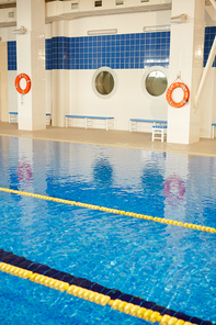 Shot of empty indoor sports swimming pool with lanes separated by yellow lines on still clear water surface and life rings hanging beside it