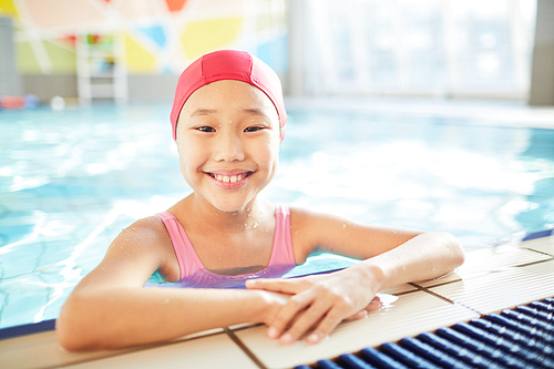 Smiling Asian schoolgirl spending leisure in modern swimming-pool