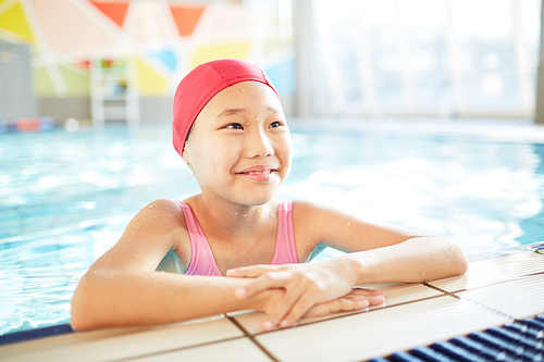 Happy Asian girl in swimwear standing in water of swimming pool during training