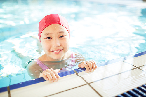 Cute little girl in swim-cap  during training in swimming-pool