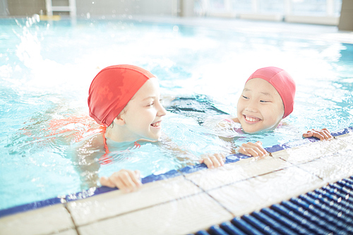 Two friendly schoolgirls having fun while practicing swimming in pool