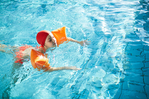 Schoolgirl swimming in pool with special inflatable pillows around her arms