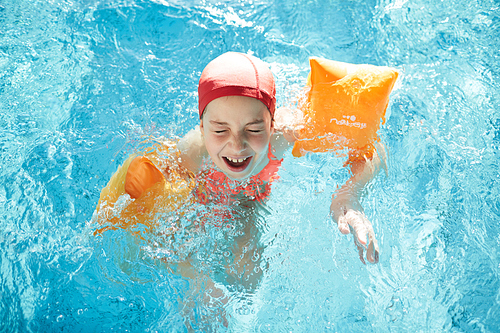 Funny girl in swimwear and special resistance pillows enjoying swimming at leisure