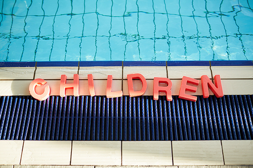 Word 'children' formed up on the floor of swimming-pool by edge of water