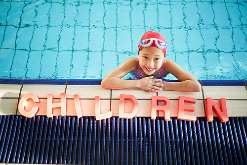 Adorable girl in swimwear  while leaning on edge of swimming-pool with word 'children'