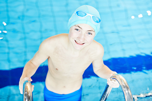 Happy boy in swimwear and goggles looking at camer while getting out of swimming-pool