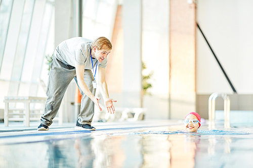 Happy trainer encouraging his young student while she swimming in pool