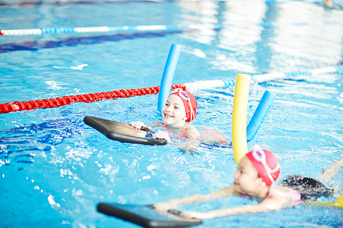 Two schoolgirls in swimwear and special swim devices learning to swim