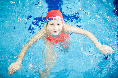 Top view of happy girl looking at camer out of clear transparent water of swimming-pool