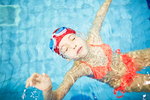 Schoolgirl in swimwear and goggles going down under water while learning to swim