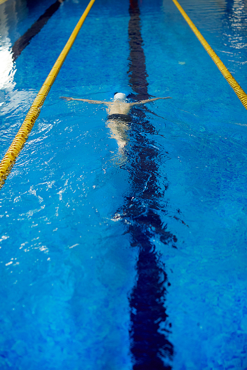 High angle shot of unrecognizable school age boy swimming fast face down underwater with large strokes in pool lane separated by yellow lines