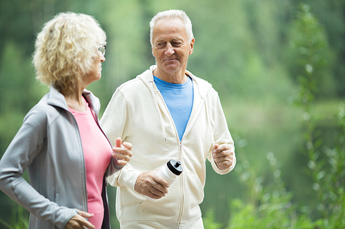 Active senior man with bottle of water looking at his wife while jogging in the morning