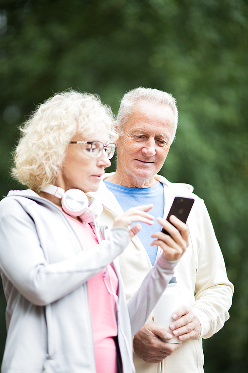 Aged man and his wife watching video of sports exercise in smartphone at break