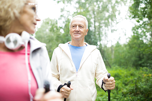 Aged grey-haired man in activewear looking at his wife while trekking in park
