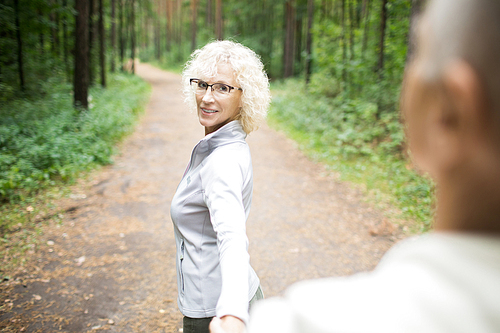 Mature woman with blond curly hair looking at her husband while leading him forwards