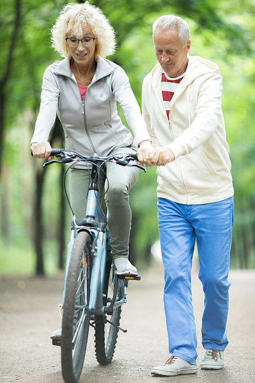 Aged man supporting his wife while teaching her to ride bicycle at leisure
