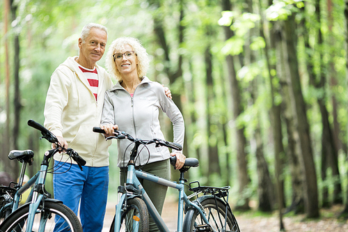 Happy active seniors with bicycles enjoying summer weekend in the forest