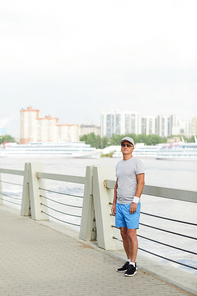 Mature man in sportswear standing by railings on bridge by riverside in the morning