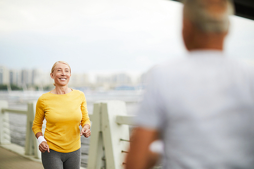 Happy aged woman smiling at man running towards her while training in urban environment in the morning