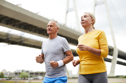 Mature sporty couple in activewear jogging together in urban environment in the morning