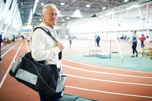Mature man with sportsbag standing by tracks on stadium on background of playing field
