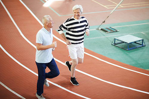 Two friendly men in activewear running down sport tracks on modern stadium and chatting on the move