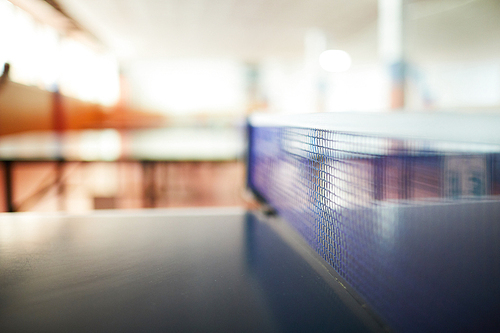 Low and wide net in the center of large table for playing tennis or ping pong in empty hall