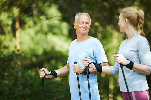 Happy active couple of seniors trekking in park or forest on summer weekend